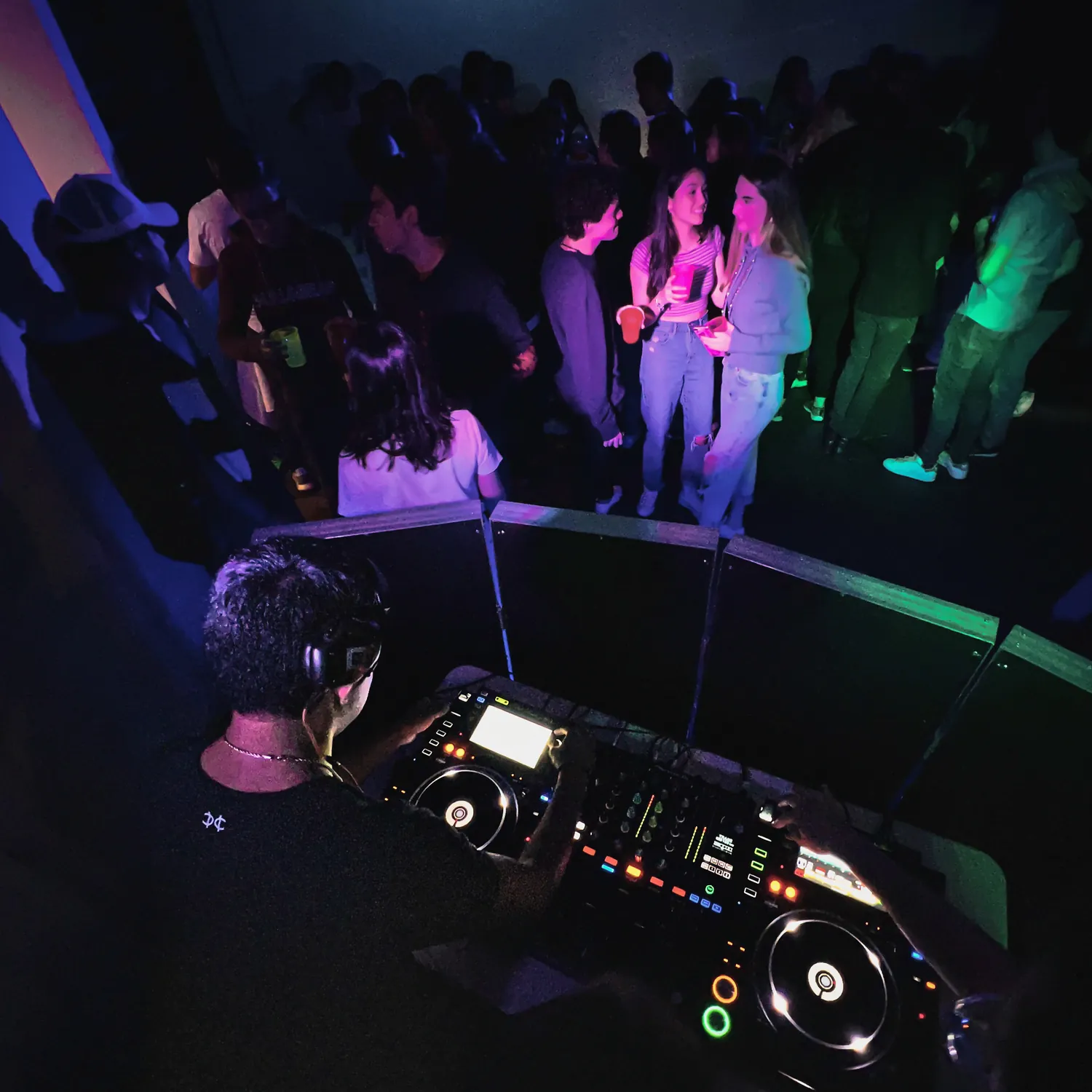 Vista desde arriba de la cabina con controlador Pioneer y gente bailando al fondo