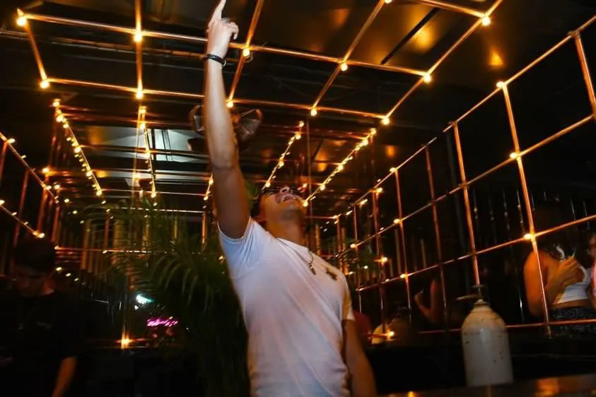 Greek con un brazo en alto en una terraza con luces cálidas