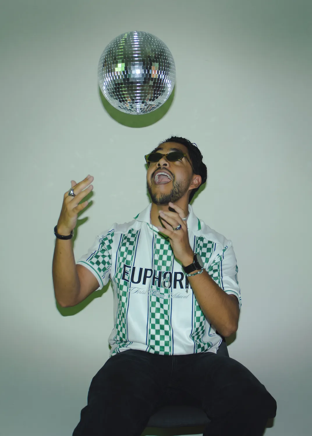 Greek con lentes y camisa de futbol bajo una bola disco