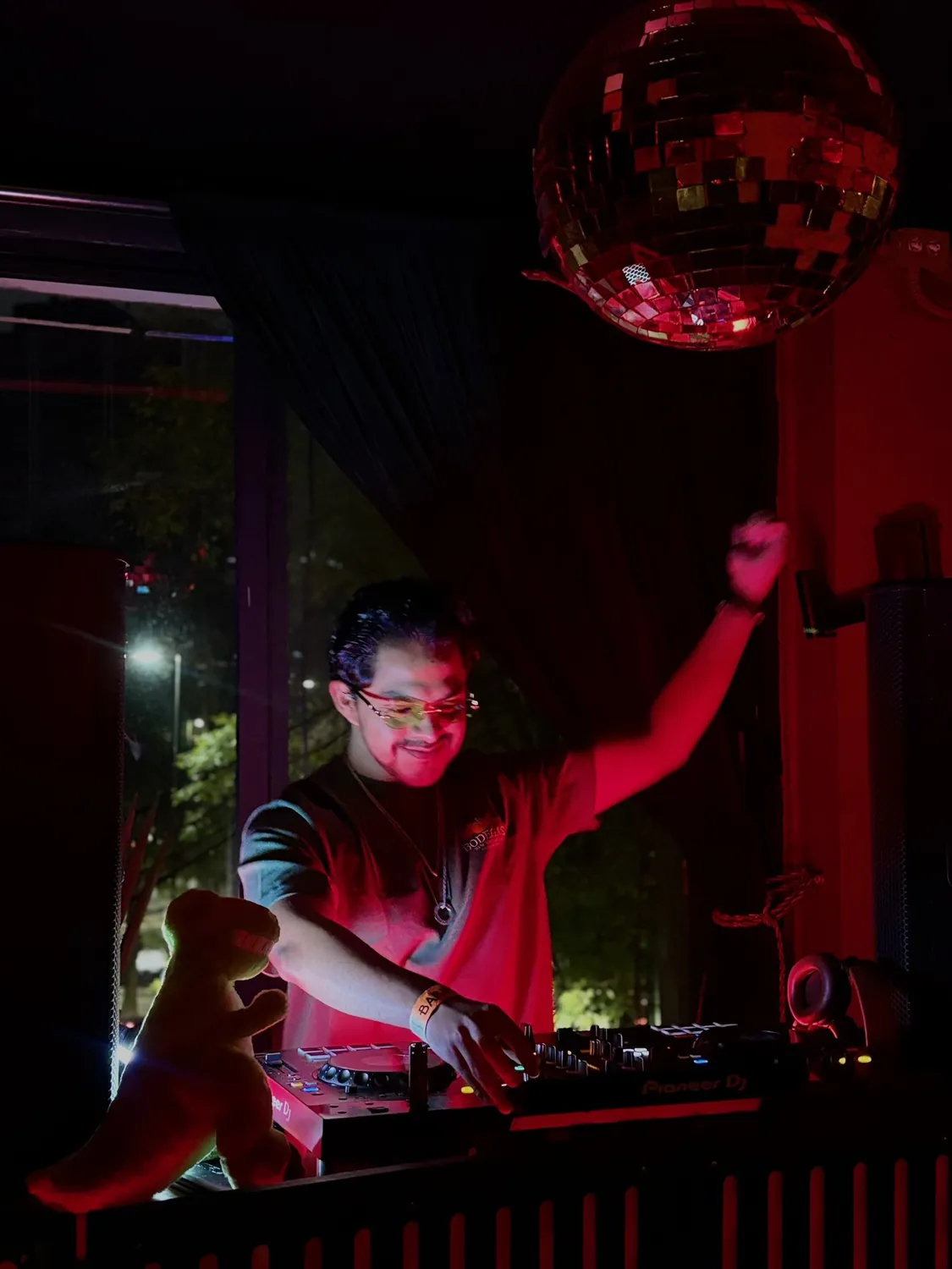 Greek con el brazo en alto bajo una bola disco con luz roja