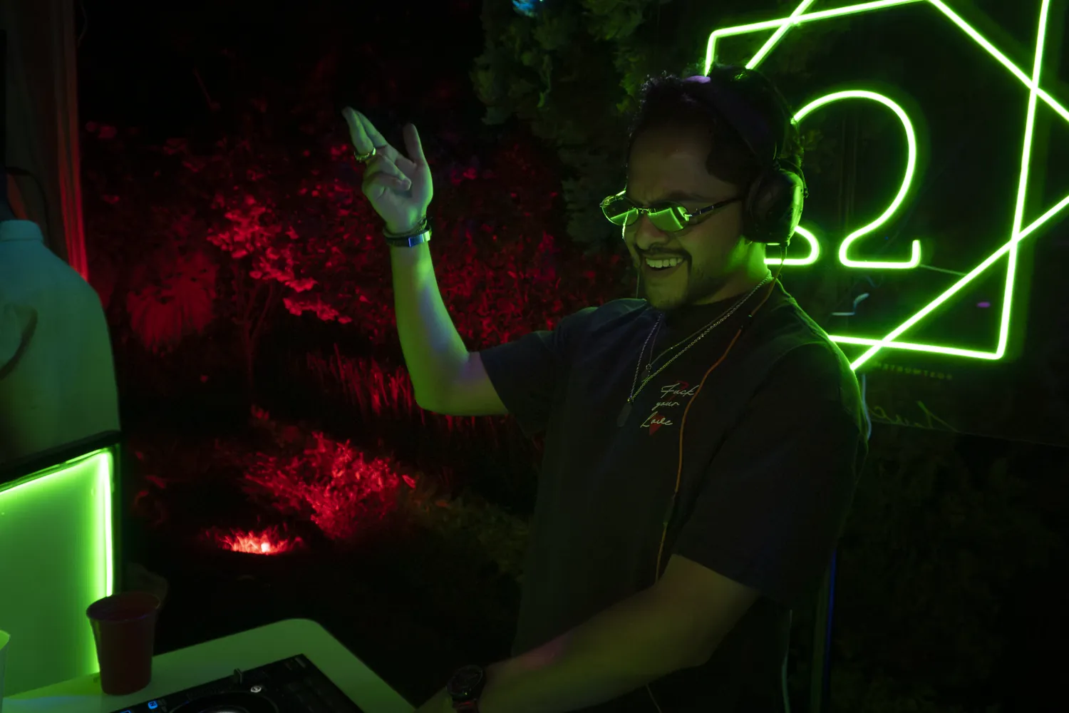 Greek sonriendo con lentes de luz verde junto al letrero Ω