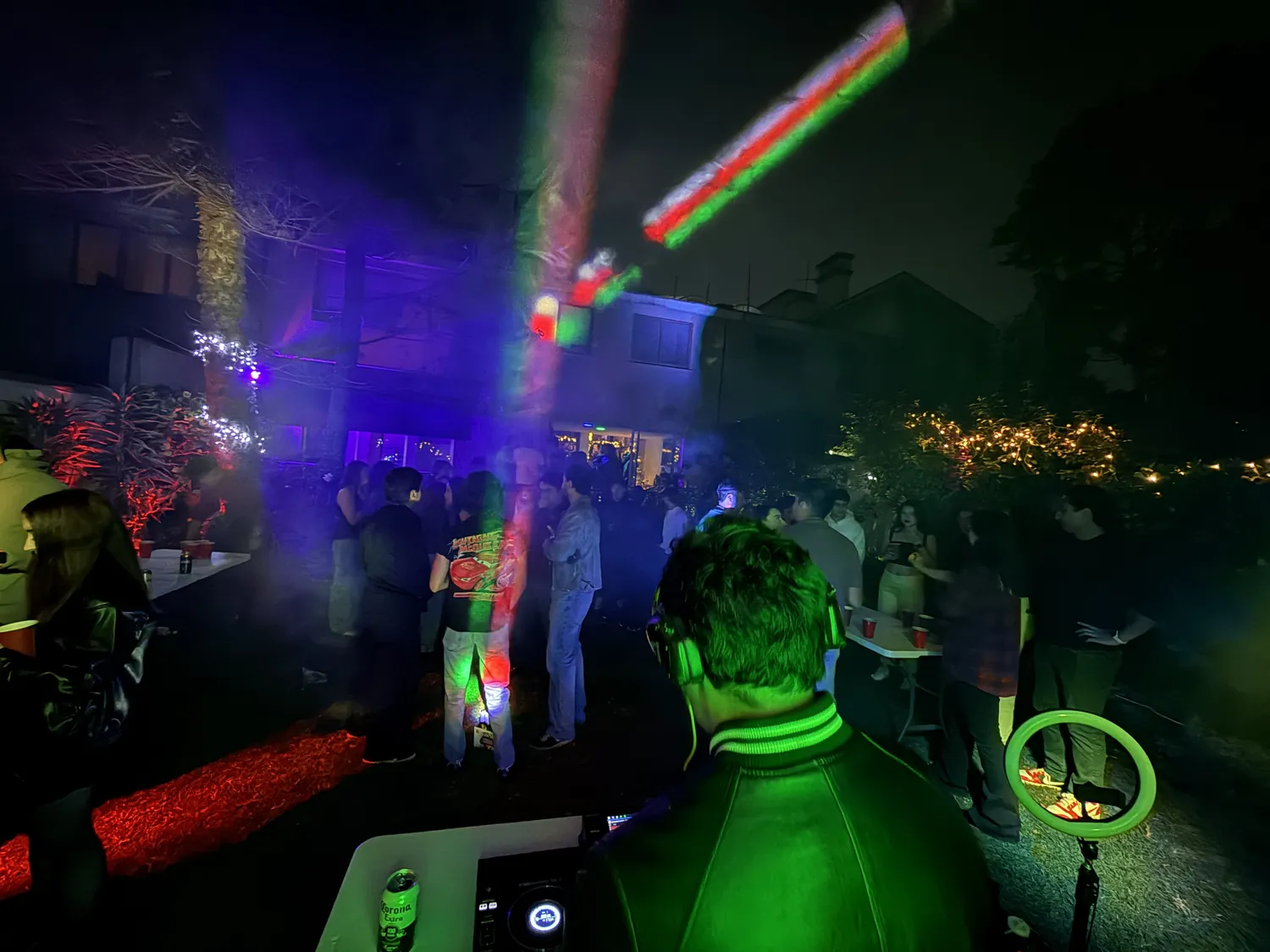 Greek de espaldas en la cabina durante una fiesta en un jardín, con luces de colores y gente bailando