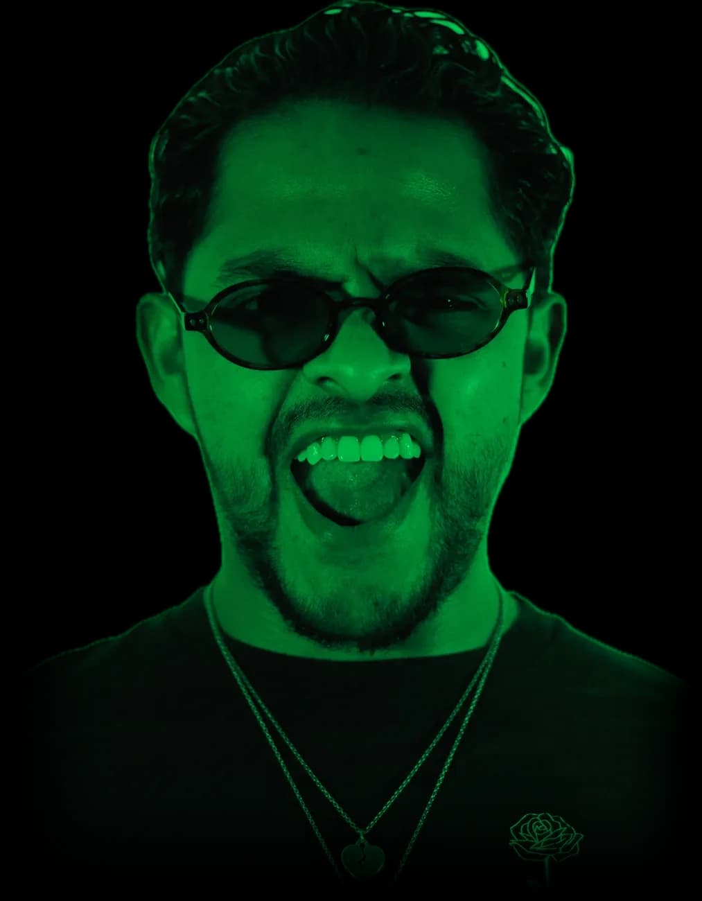 Retrato de Greek con lentes de sol, sonriendo y sacando la lengua bajo luz verde neón
